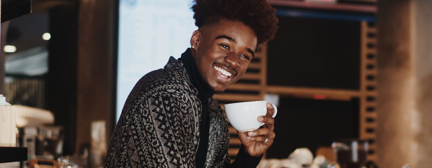young man smiles in a local cafe with a cup of coffee
